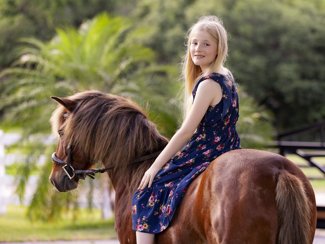 A girl riding a chestnut pony bareback, looking back over her shoulder